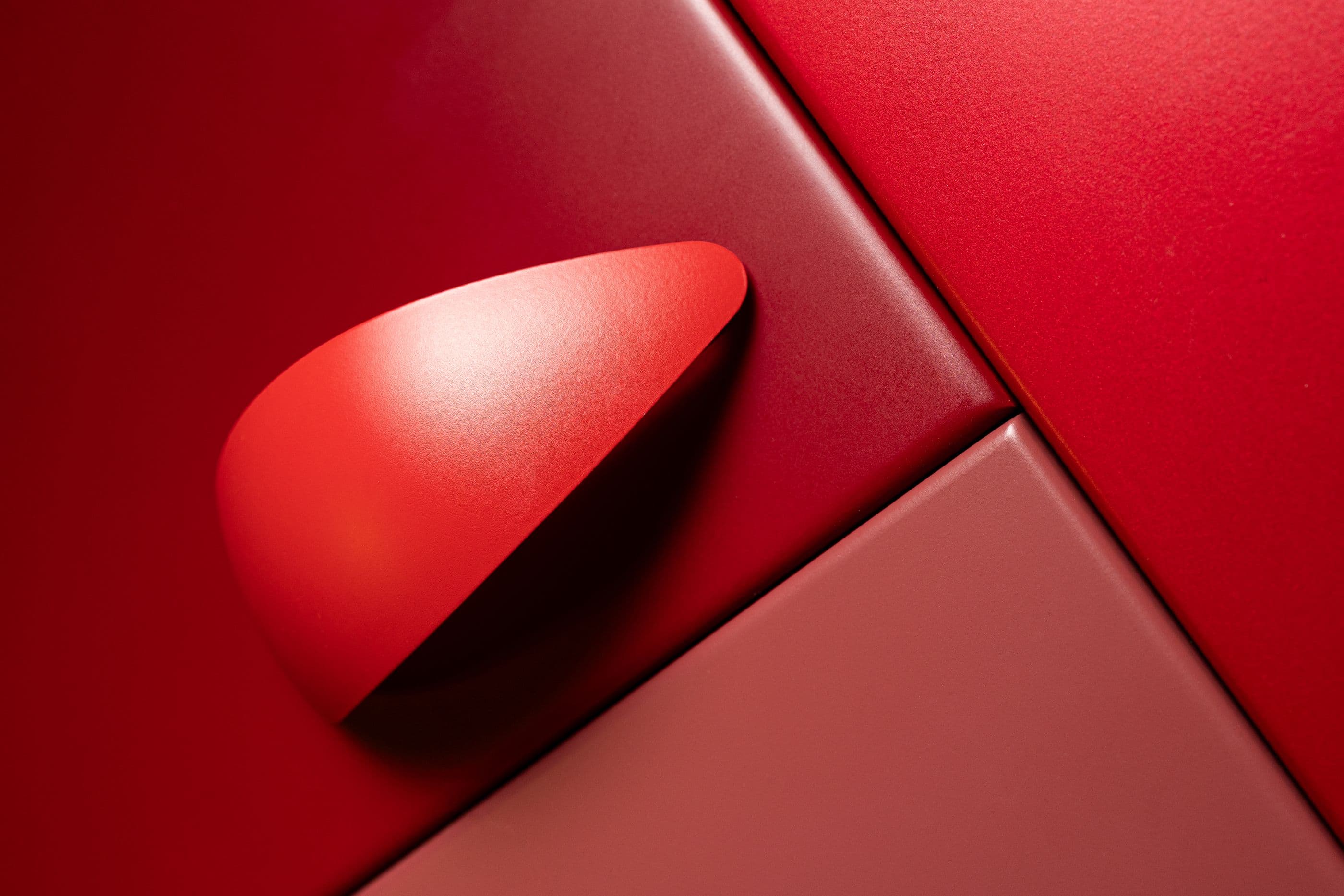 Painéis laqueados em vermelho profundo com puxador curvo na mesma cor, sob luz lateral